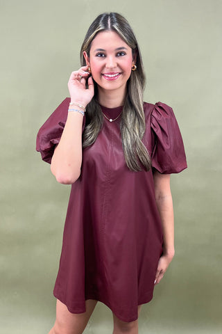 Woman wearing a burgundy dress with puffed sleeves against a green background