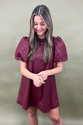 Woman wearing a burgundy dress with puff sleeves against a plain background
