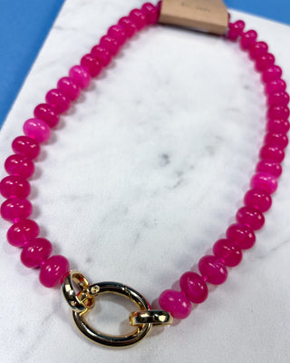 A beaded necklace made of glossy hot pink round beads with a polished gold-tone split ring clasp,