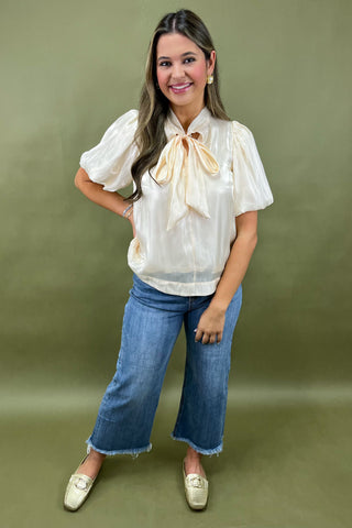 Woman wearing a white blouse with a bow and blue jeans against a green background