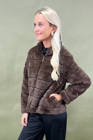 Woman wearing a brown faux fur jacket against a green background