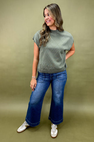 Woman wearing a green textured top and blue jeans on a beige background