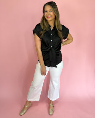 Woman wearing a black top and white pants against a pink background