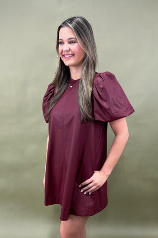 Woman wearing a burgundy dress with puff sleeves against a green background