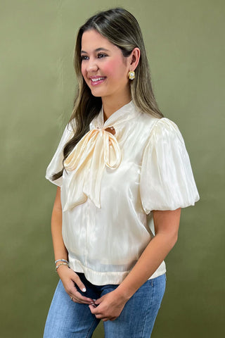 Woman wearing a white blouse with a bow and blue jeans against a green background