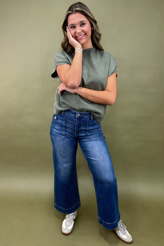 Woman wearing a green top and blue jeans against a green background