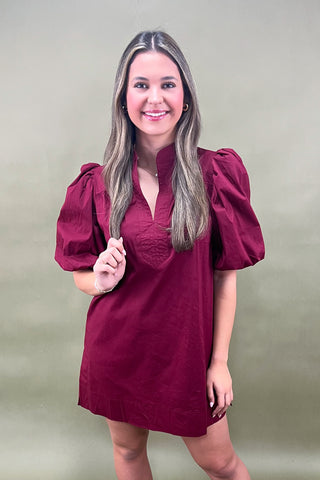 Woman wearing a burgundy dress with puff sleeves against a plain background
