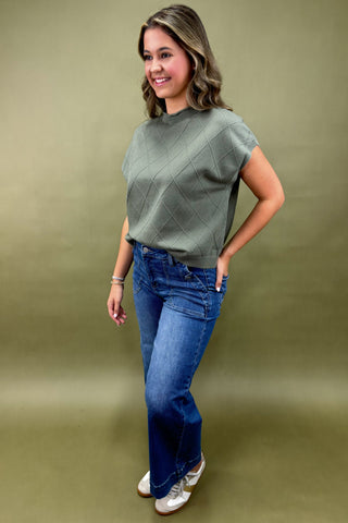 Woman wearing a green top and blue jeans against a green background