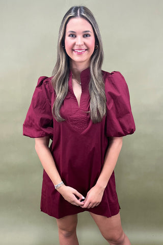 Woman wearing a burgundy dress with puff sleeves against a plain background