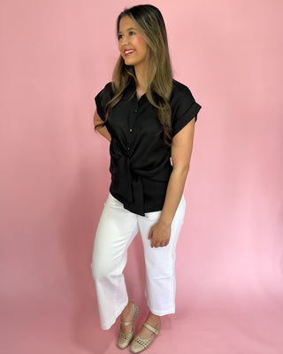 Woman wearing a black shirt and white pants against a pink background