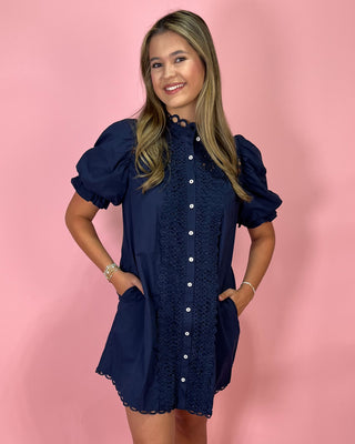 Woman wearing a navy dress with white buttons against a pink background