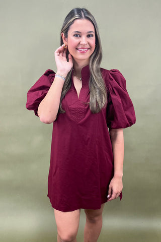 Woman wearing a burgundy dress with puff sleeves against a green background