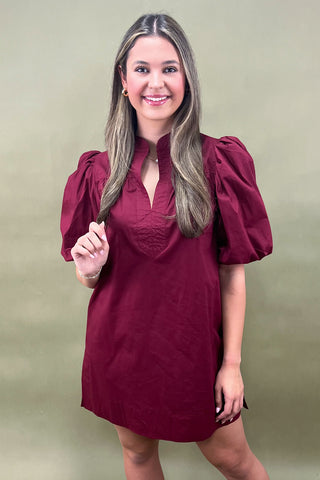 Woman wearing a burgundy dress with puff sleeves against a beige background