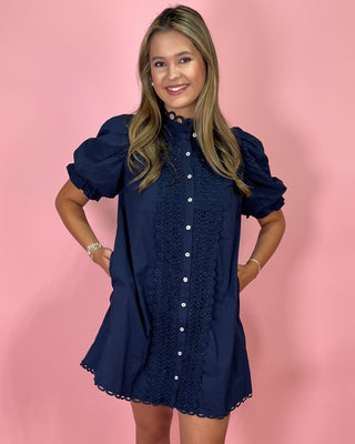 Woman wearing a navy blue dress with white buttons against a pink background