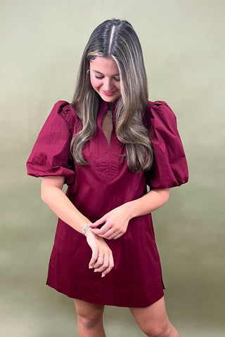 Woman wearing a burgundy dress with puff sleeves against a plain background