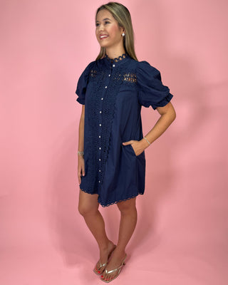 Woman wearing a navy dress with lace details on a pink background