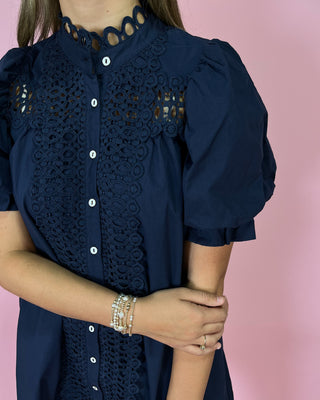 Navy blue dress with intricate lace detailing on a pink background