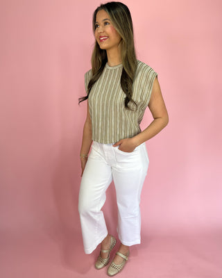 Woman wearing a striped top and white pants against a pink background