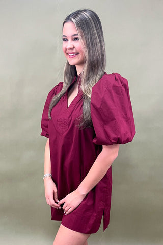 Woman wearing a burgundy dress with puff sleeves against a plain background