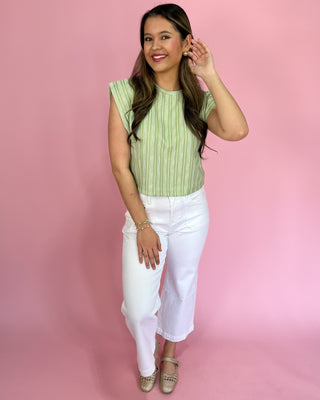 Woman wearing a green striped top and white pants against a pink background