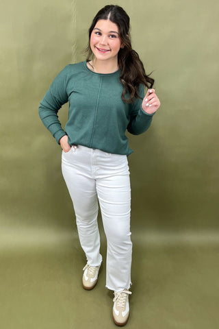 Woman wearing a green sweater and white pants against a green background