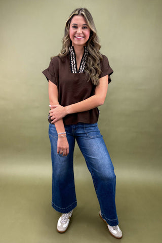 Woman wearing a brown top and blue jeans against a green background