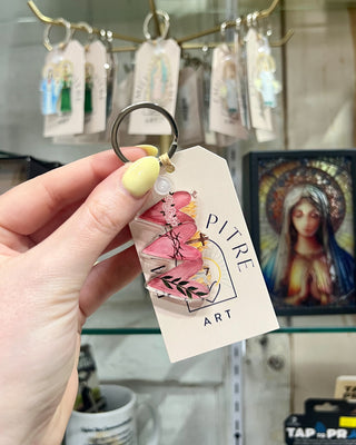 Hand holding a keychain with a 'Pitre Art' tag in front of a store display.