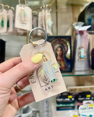 Keychain with religious figure on a tag held by a hand in a store setting.