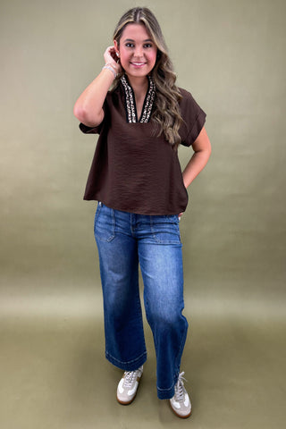 Woman wearing a brown top and blue jeans against a green background
