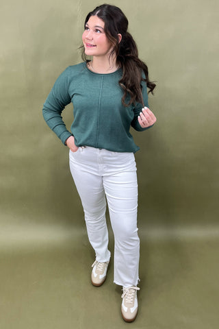Woman wearing a green sweater and white pants against a green background