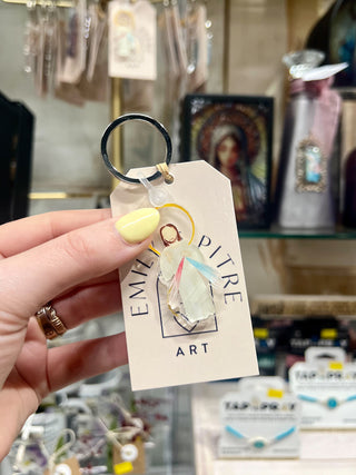 Keychain with 'Emilie Pitre Art' tag held by a hand in a store setting