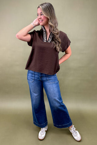 Woman wearing a brown top, blue jeans, and white sneakers on a green background