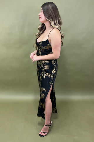 Woman wearing a black and gold dress with a slit on a green background