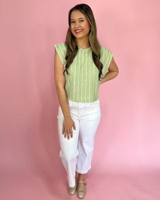 Woman wearing a green striped top and white pants against a pink background