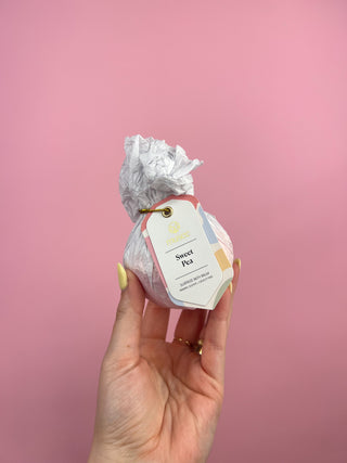 Hand holding a wrapped product with a label against a pink background
