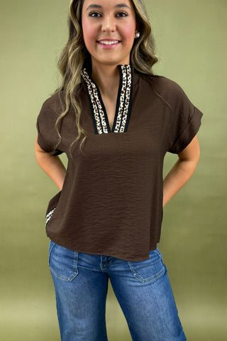 Woman wearing a brown short-sleeve top with decorative trim against a green background