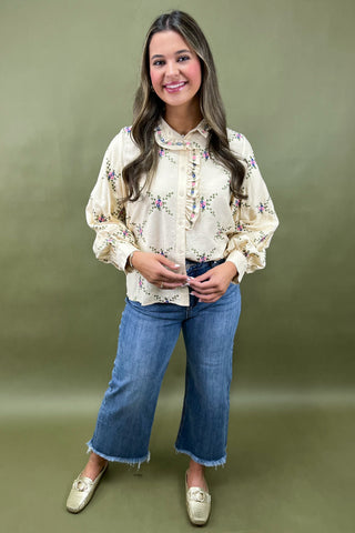 Woman wearing a floral blouse and blue jeans against a green background
