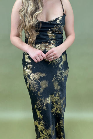 Woman wearing a black and gold patterned dress against a green background