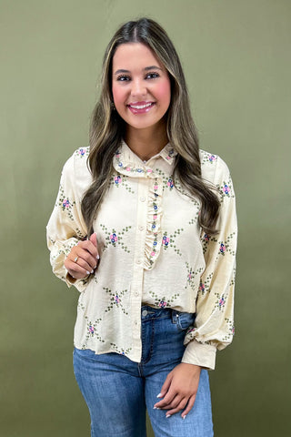 Woman wearing a cream blouse with floral patterns against a green background