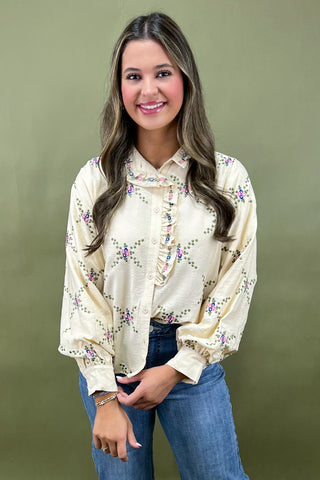 Woman wearing a cream floral blouse and blue jeans against an olive green background