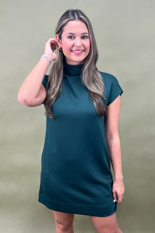 Woman wearing a teal dress against a plain background