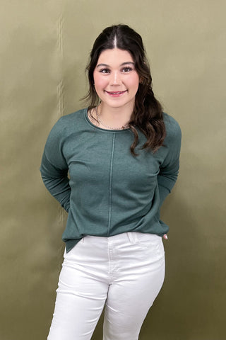 Woman wearing a green sweater and white pants against a beige background