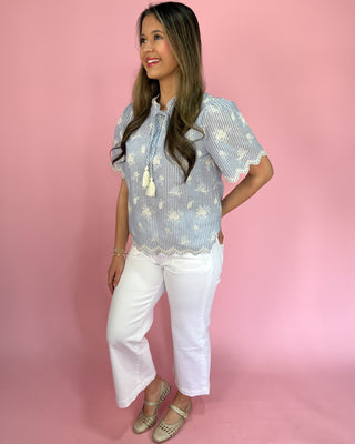 Woman wearing a blue and white patterned blouse with white pants against a pink background