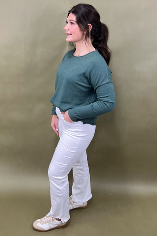 Woman wearing a green sweater and white pants against a beige background