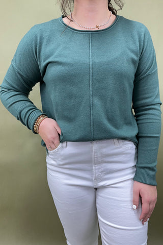 Person wearing a teal sweater and white pants against a beige background