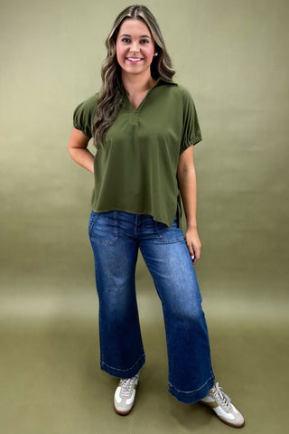 Woman wearing an olive green top and blue jeans against a green background