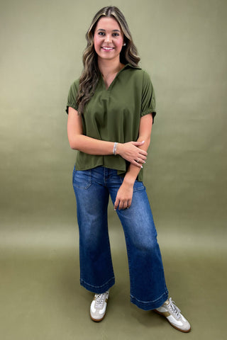 Woman wearing an olive green top and blue jeans against a green background