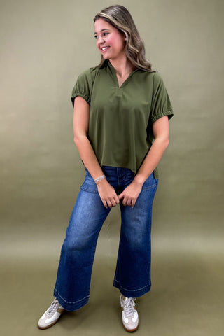 Woman wearing an olive green shirt and blue jeans against a beige background