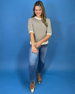 a beige and dark brown horizontally striped short-sleeve top with a curved hem, paired with blue jeans and metallic gold flats
