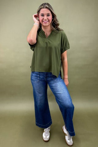 Woman wearing an olive green top and blue jeans against a green background
